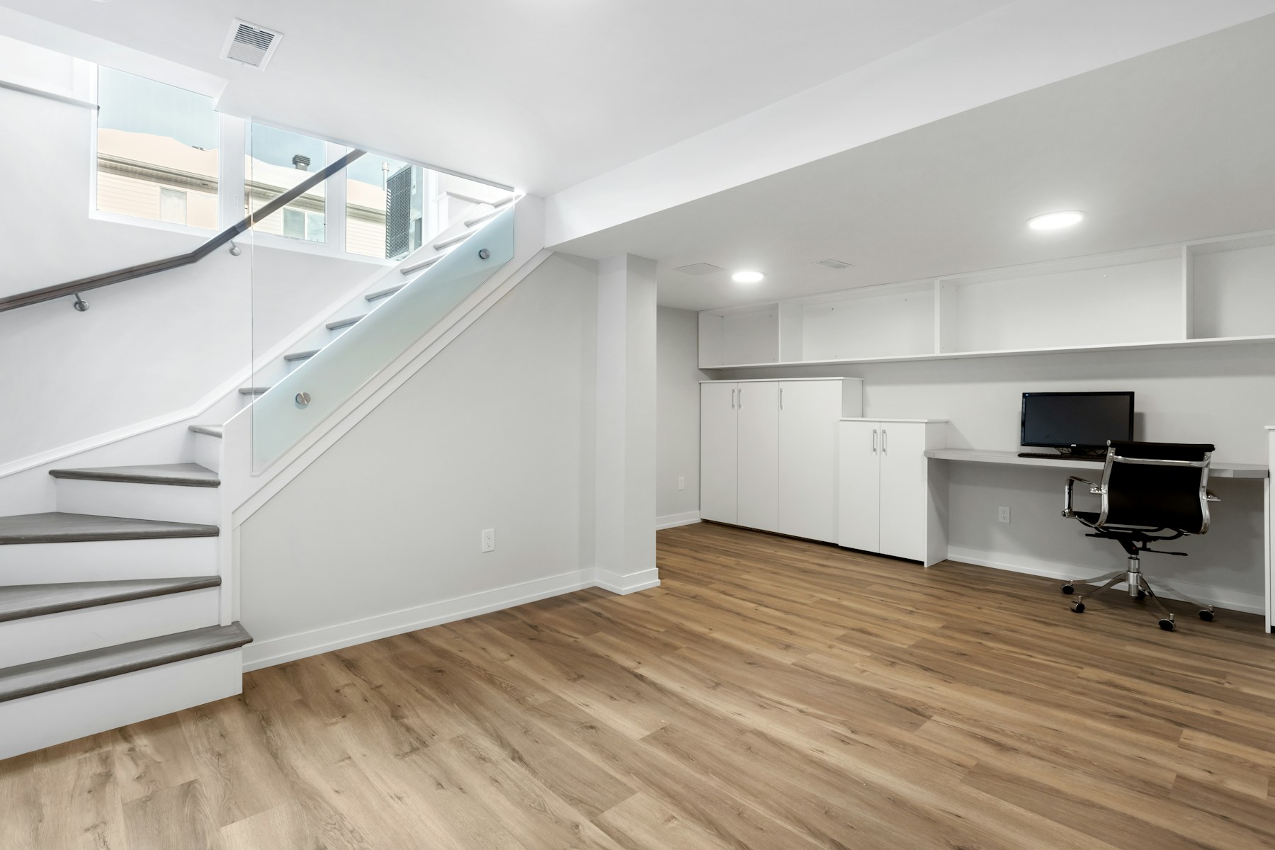 A basement with a desk, computer, and stairs
